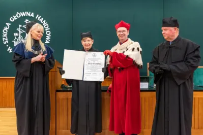 Cztery osoby w togach. Profesor Urszula Grzelońska uroczyście odbiera dyplom z rąk rektora.