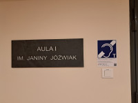 Widok na tablicę z nazwą Auli I w bud. C oraz z piktogramem pętli indukcyjnej