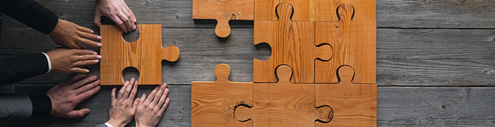 dłonie trzech osób układajace drewniane puzzle