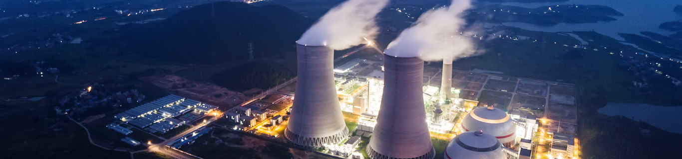Elektrownia jądrowa z lotu ptaka po zmroku z oświetloną infrastrukturą energetyczną i chłodniami kominowymi