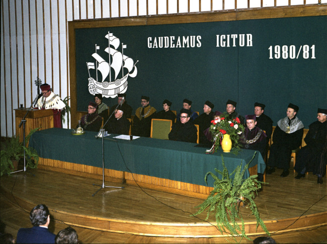 Inauguracja roku akademickiego 1980/1981  Przemawia JM Rektor prof. Stanisław Nowacki. W pierwszym rzędzie od lewej profesorowie: Witold Sierpiński – prorektor, Kazimierz Secomsk – członek rzeczywisty PAN, Wiesław Sadowski – członek korespondent PAN, Barbara Prandecka – prorektor, Wojciech Wrzosek – prorektor. W drugim rzędzie od lewej profesorowie: Irena Fierla – dziekan Wydziału Ekonomiki Produkcji, Leszek Gilejko – dziekan Wydziału Ekonomiczno-Społecznego, Alicja Sajkiewicz – przedstwicielka Wydziału Eko