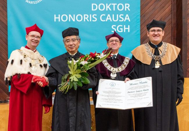 rektor SGH dr hab. Piotr Wachowiak, prof. SGH ściska dłoń prof. Mamoru Kaneko, prof. Kaneko trzyma w drugiej dłoni bukiet kwiatów, prorektor do spraw współpracy z zagranicą dr hab. Jacek Prokop, prof. SGH pokazuje do zdjęcia otwarty dyplom doktora honoris causa, obok stoi dziekan Kolegium Gospodarki Światowej prof. dr hab. Mariusz Próchniak