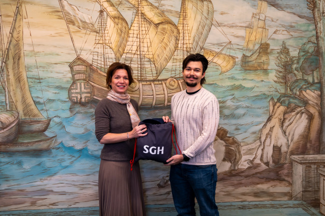 Prorektor ds. rozwoju wręcza pakiet upominków zwycięzcy w konkursie Hasło na dobry start.